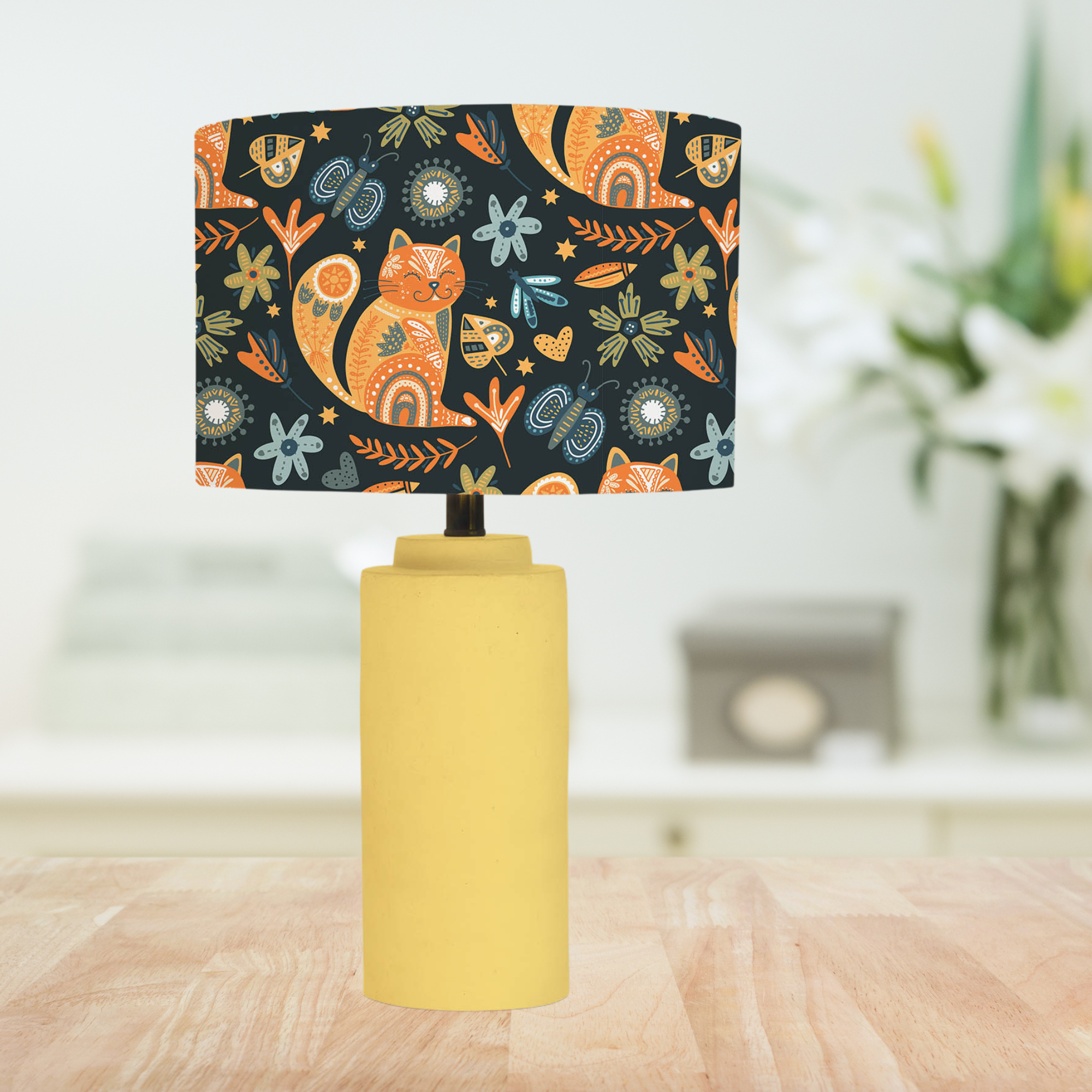 This handmade lampshade features a boho inspired pattern of content little pussy cats among leaves, florals and butterflies in tones of orange, blue and green on a black background.