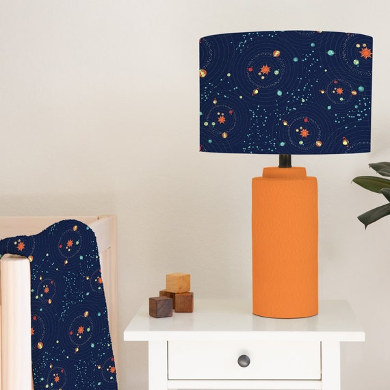 Children's bedroom and nursery lampshade lightshade for ceiling fitting or lamp base featuring a space scene of assorted planets in a solar system in oranges, reds, yellows and greens on a dark blue background.